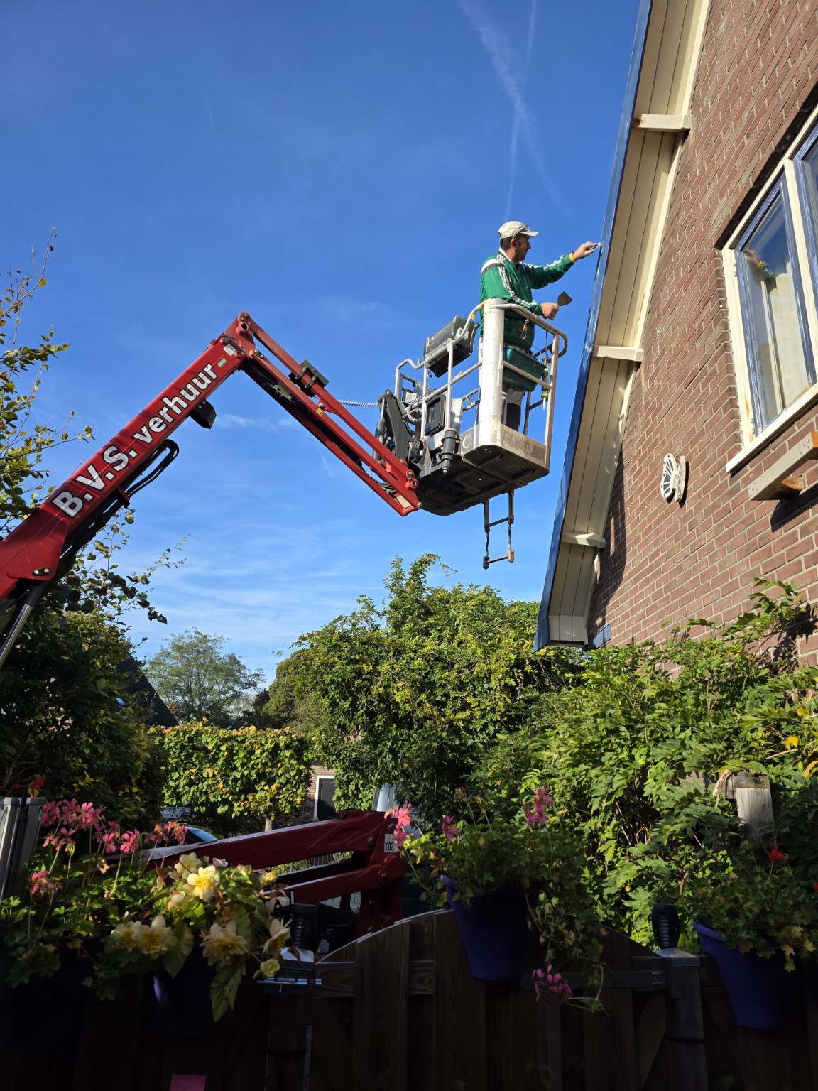 Schilder op een hoogwerker tijdens de voorbereiding van een blauw boeideel aan een bakstenen woning