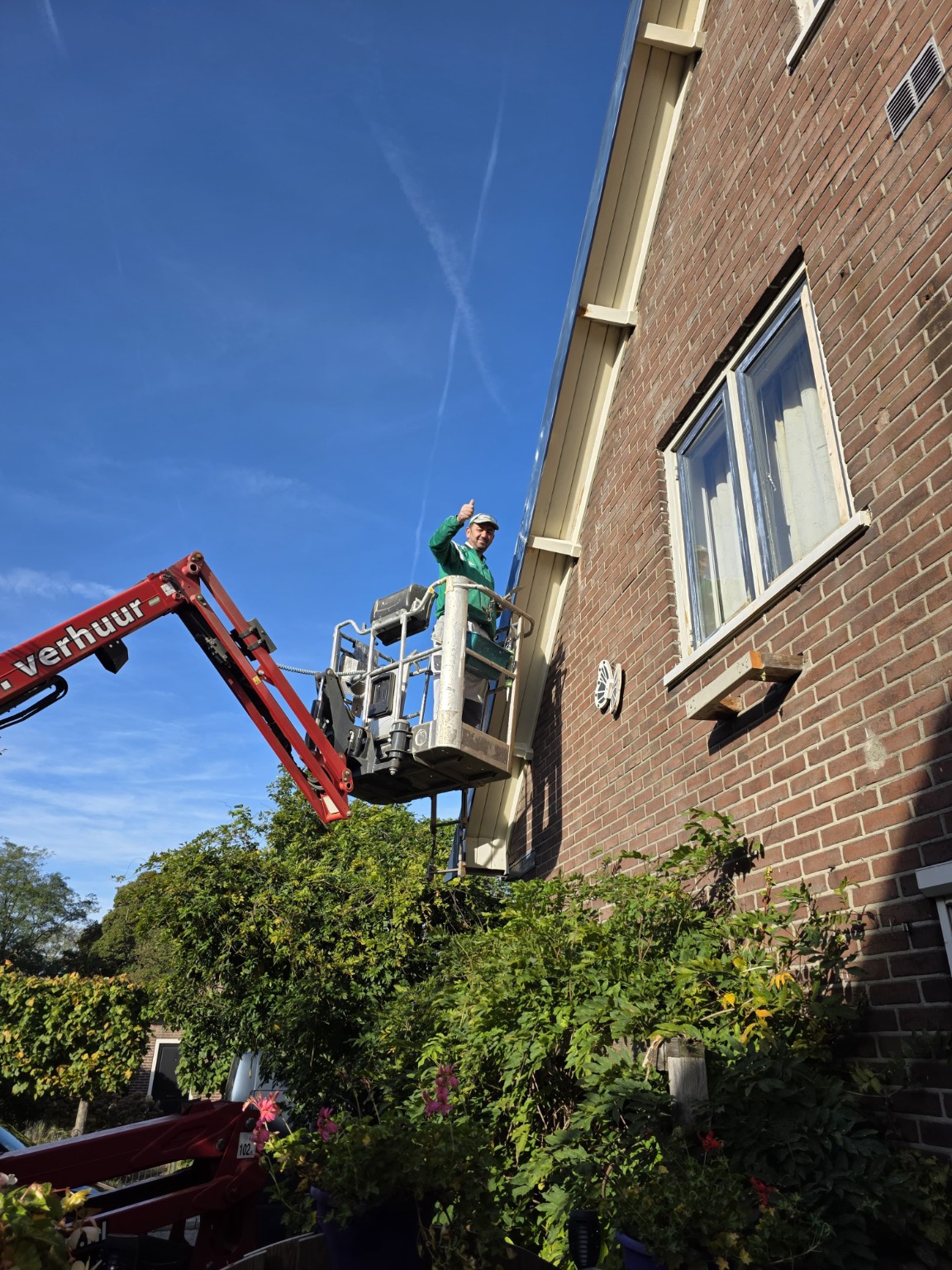 Schilder op een hoogwerker naast de gevel van een woning, met een duim omhoog