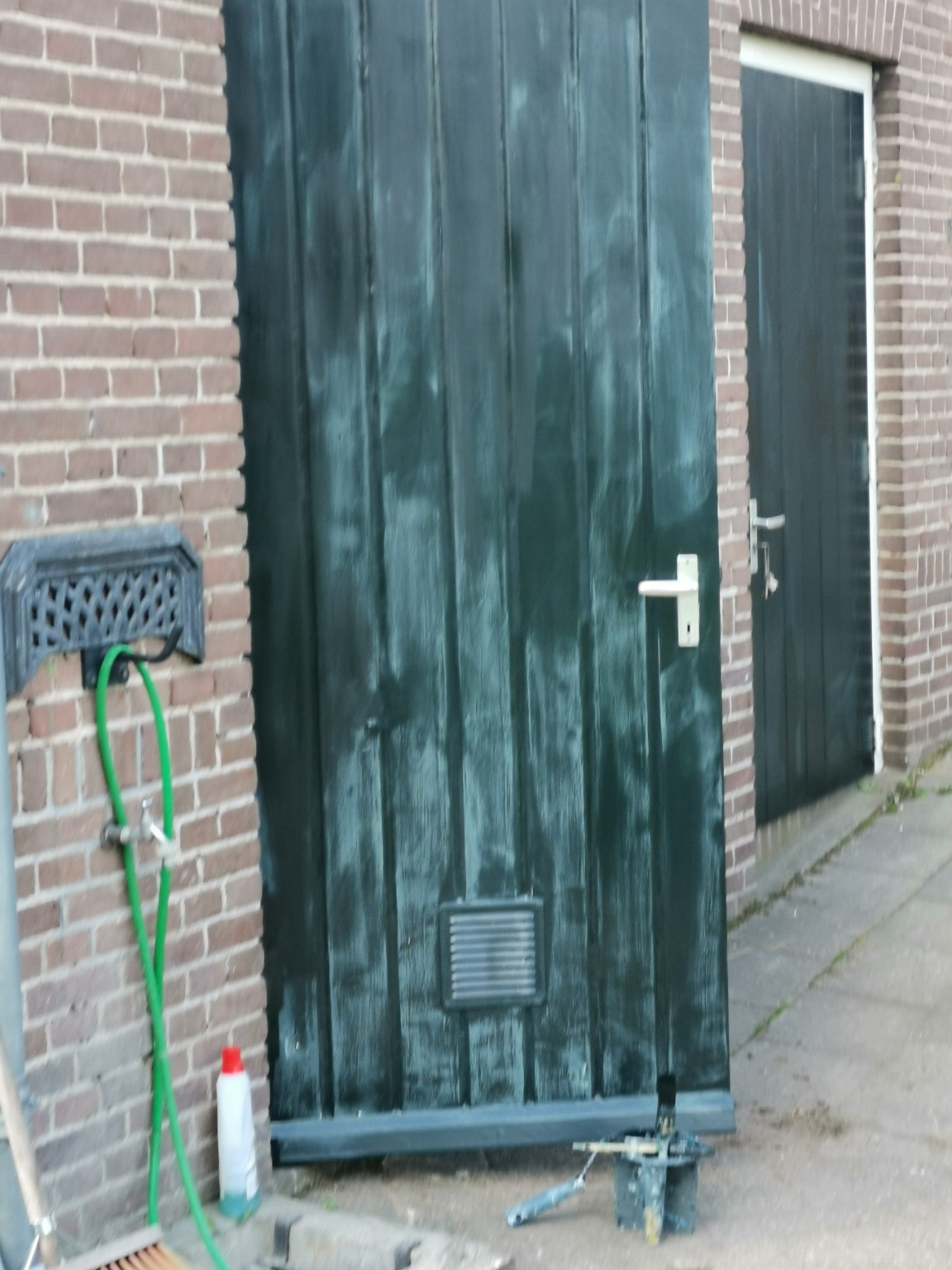 Groene houten buitendeur na het aflakken met een glanzende verflaag, in een wit kozijn naast een bakstenen muur