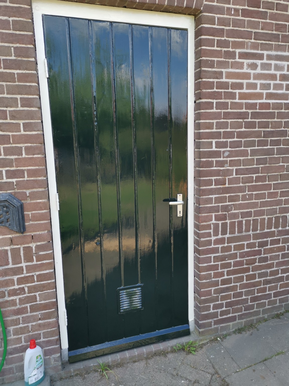 De groene houten buitendeur geschuurd en voorbereid vóór het aflakken, met gereedschap naast de deur
