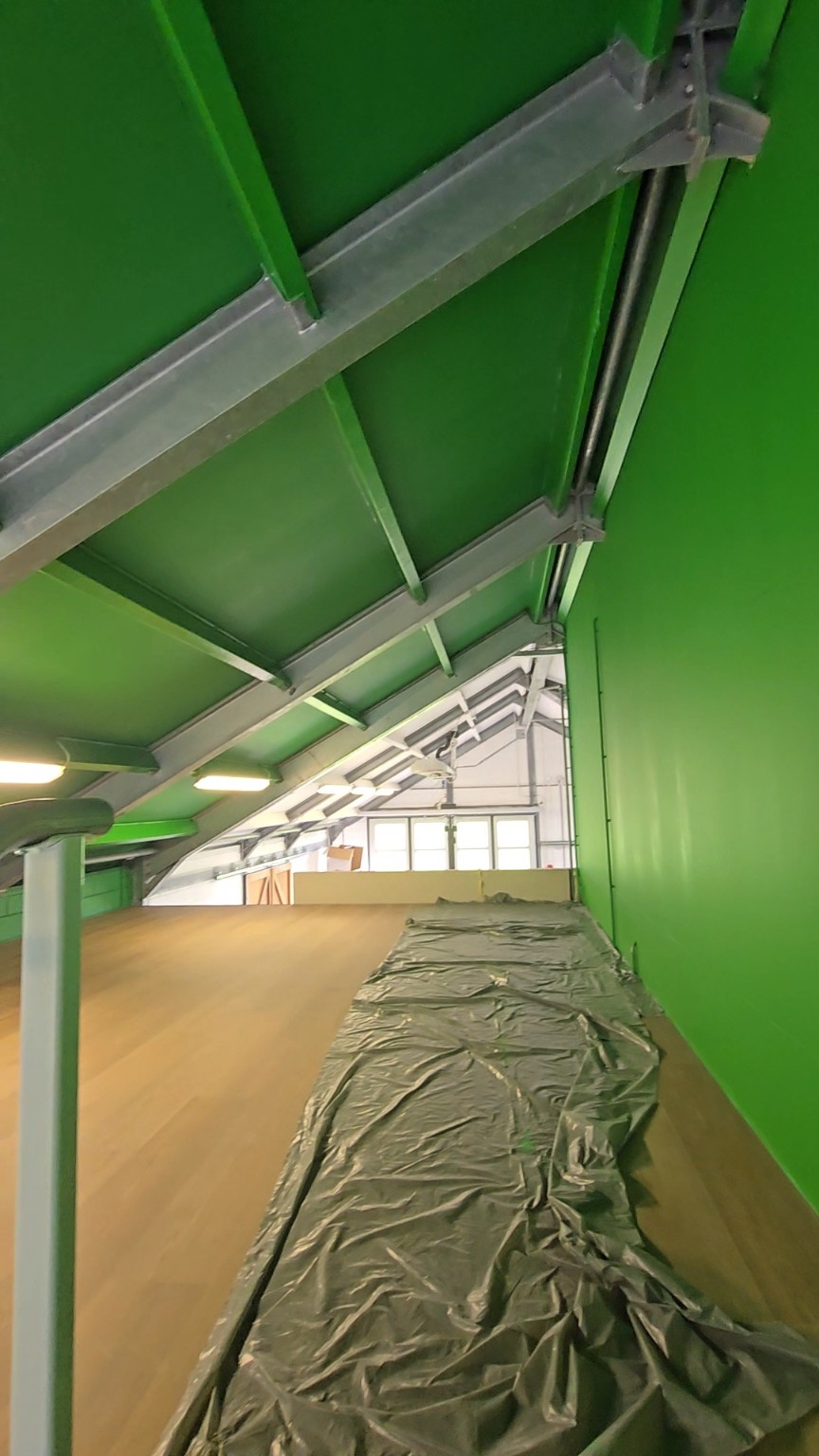 Werkruimte na het schilderwerk met groene wanden en een groen schuin plafond, stalen balken en afdekfolie op de vloer